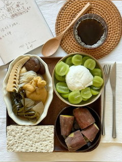 Overhead view of Korean food dishes including stew, grapes, sweet potato, and dipping sauce on a wooden tray