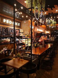 Cozy coffee shop interior with warm lighting, brick walls, bar stools, and hanging plants at night