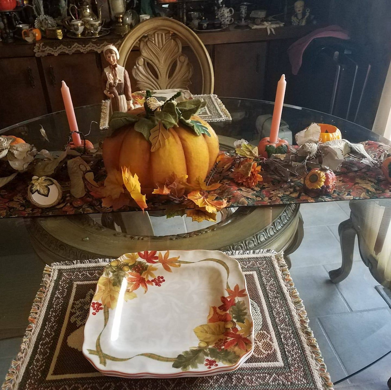 Autumn dining table with pumpkin centerpiece, candles, fall leaves, and a floral serving plate