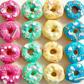 Grid of 16 pastel-colored donuts with colorful glazes and white sprinkles arranged in four rows