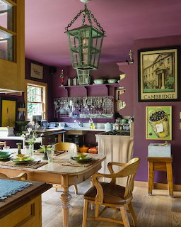 Kitchen dining room with purple walls, wooden table set for meal, hanging green lantern, vintage posters