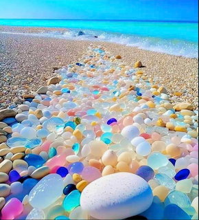 Colorful sea glass pieces and smooth pebbles forming a path on beach toward turquoise ocean