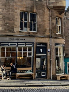 Stone cafe storefront on a city street with large windows and pedestrians walking by