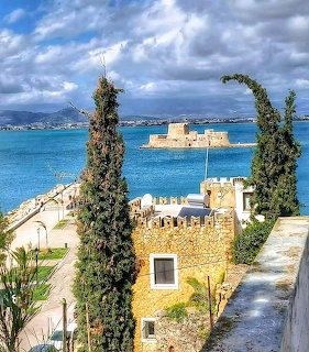 Bourtzi castle fortress in Nafplio harbor with cypress trees and stone buildings under cloudy sky