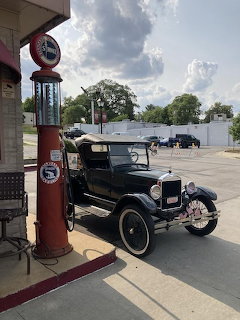 Black 1926 Ford roadster pickup next to a red vintage gas pump at an old-style gas station