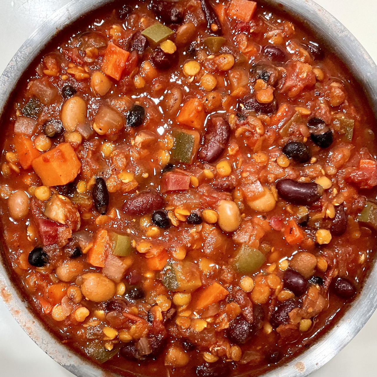 Close-up of bean chili in a pot with mixed beans, tomatoes, carrots, and vegetables