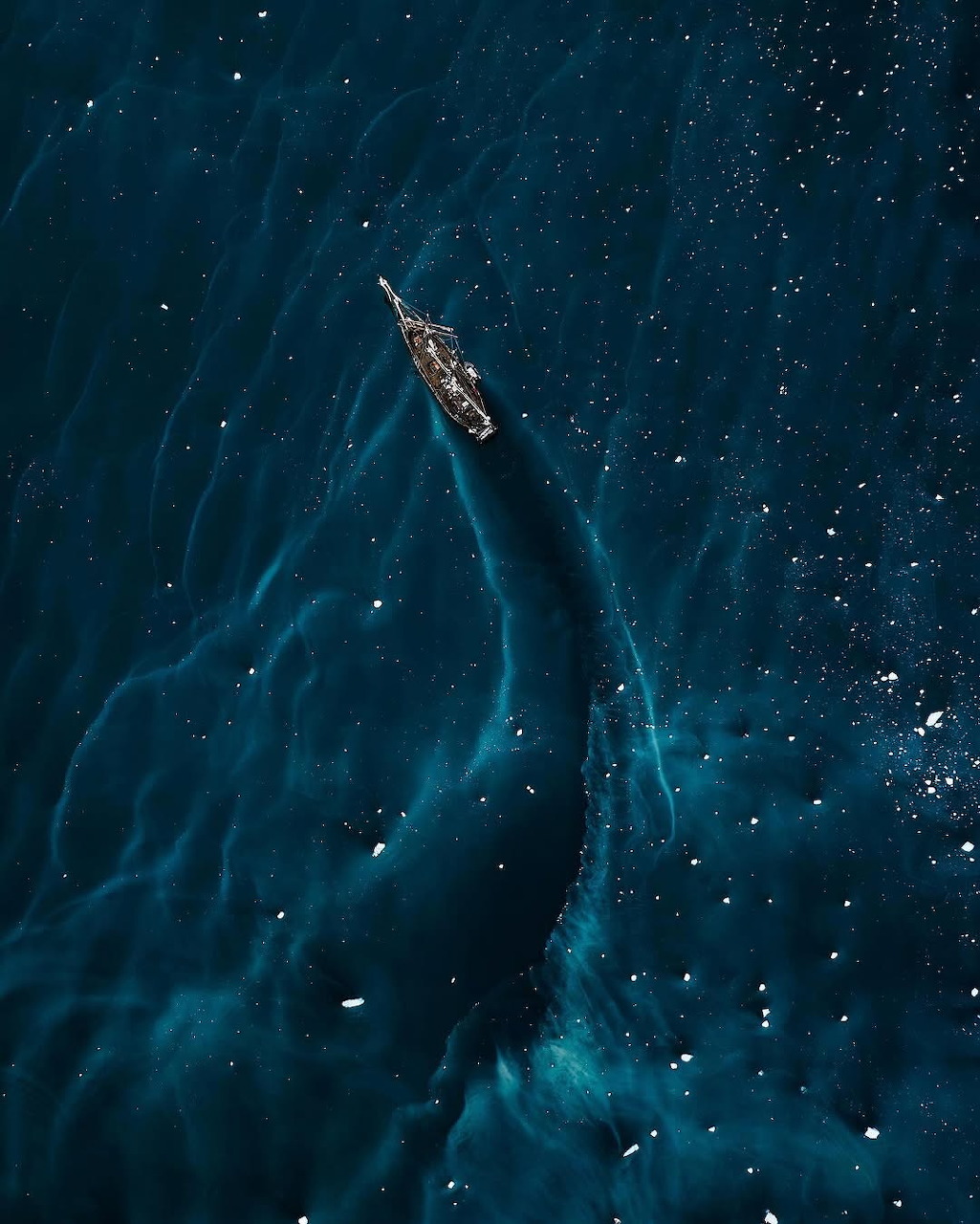 Aerial view of a lone boat sailing through dark blue ocean water with a white wake trail