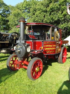 Antique steam wagon with red body, yellow wheels, and tall black chimney on grass lawn