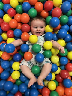 Smiling baby lying in a colorful ball pit surrounded by plastic balls