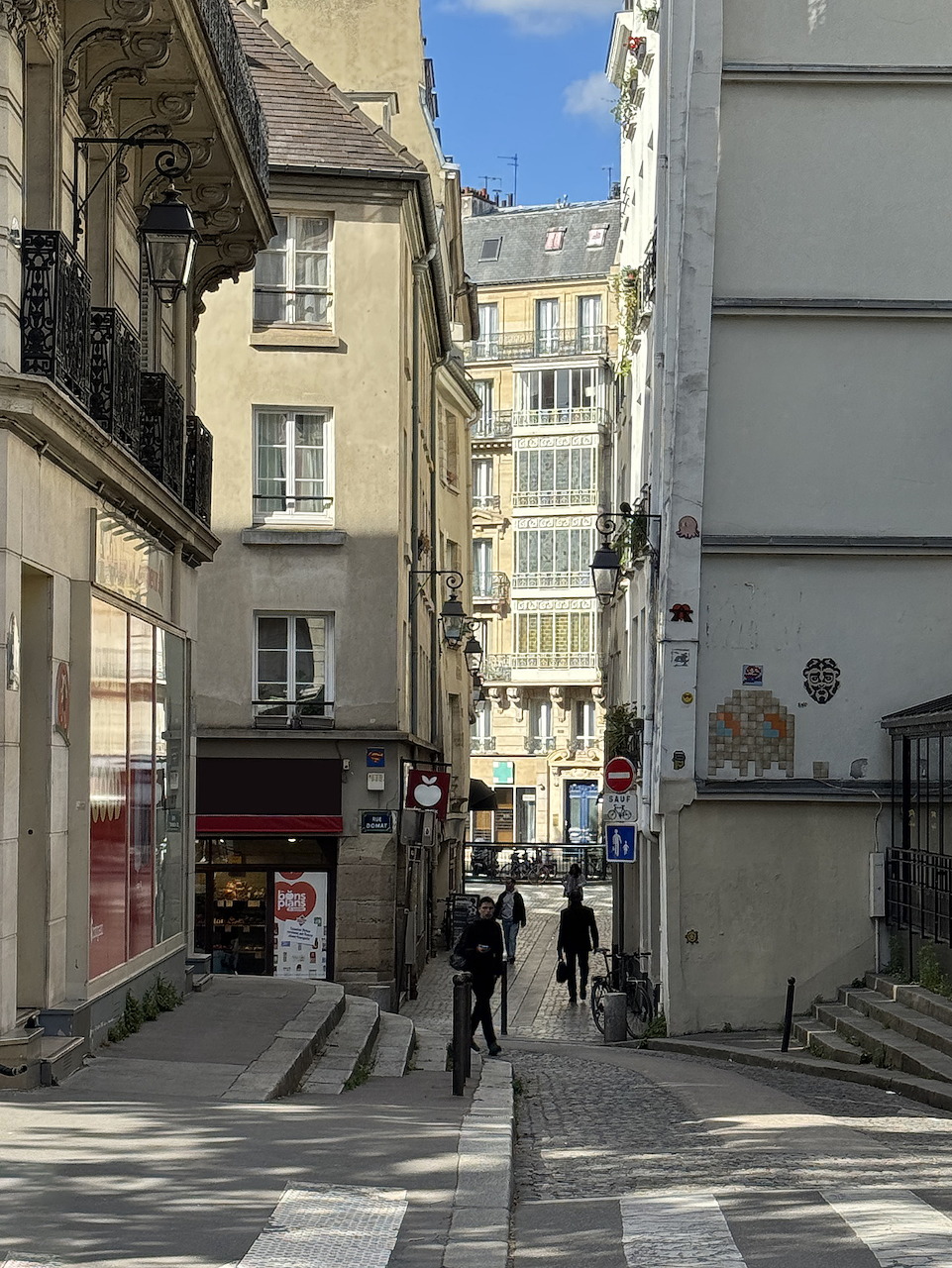 Narrow Paris street with old beige buildings, pedestrians, and clear blue sky