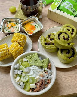 Tabletop spread of corn, grape salad, baked dishes, green pastries, and a drink
