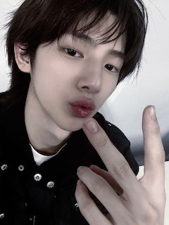 Close-up selfie portrait of a young person with short dark hair making a hand gesture