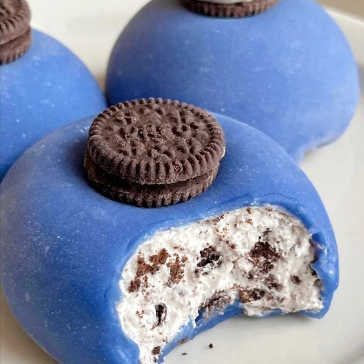 Blue mochi desserts with cookies and cream filling, one bitten to show white ice cream interior with chocolate cookie pieces