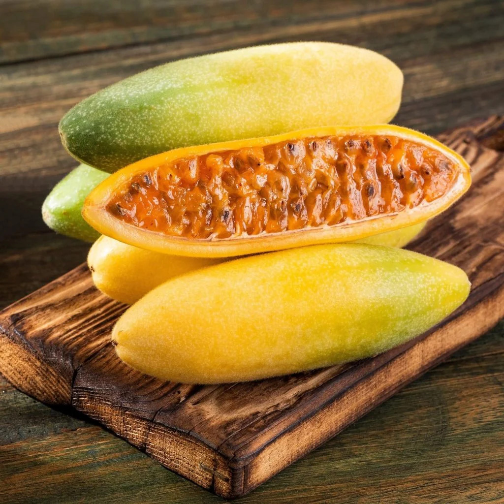 Whole and halved banana passion fruits displaying orange seedy interior on rustic wooden cutting board
