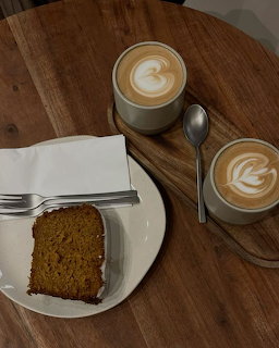 Two cappuccinos with latte art and a slice of cake on a round wooden table