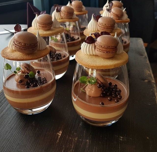 Layered dessert cups with macarons, chocolate pearls, and mint garnish on wooden table