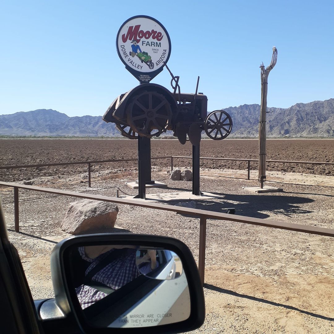 Vintage Arizona farm sign silhouette with tractor against desert mountains, viewed from car mirror