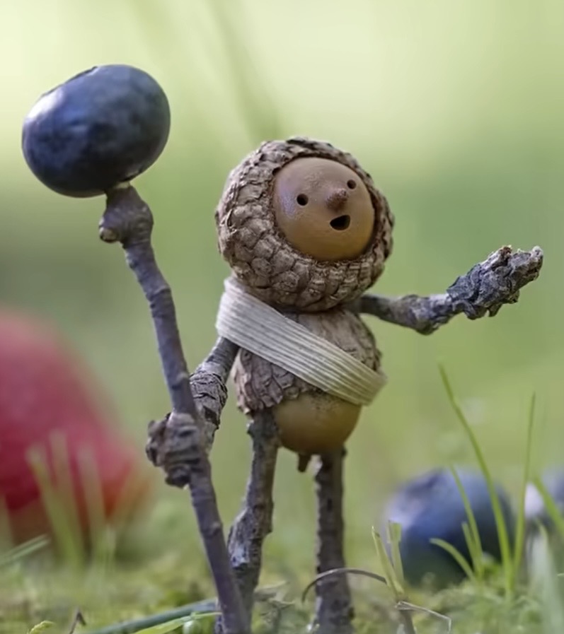 Small becorn figure in grass holding a blueberry-topped staff