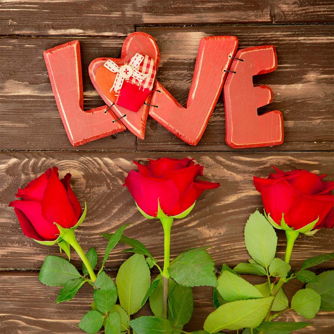 Red roses arranged below decorative LOVE letters with heart ornament on wooden planks