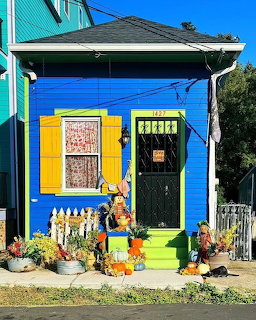 Bright blue tiny house with yellow shutters decorated with pumpkins and scarecrow for Halloween
