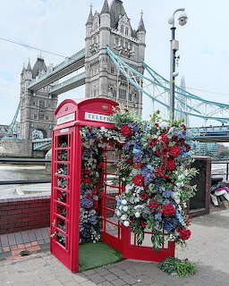 Red London telephone box decorated with flowers in front of Tower Bridge