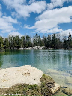Calm turquoise lake surrounded by conifer forest and rocky limestone shoreline under blue sky with clouds