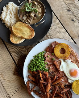 Breakfast plate with fried egg, bacon, peas, pineapple, and fries on wooden table