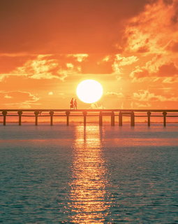 Bright orange sunset over ocean with silhoueted figures on a pier and sun reflection on water