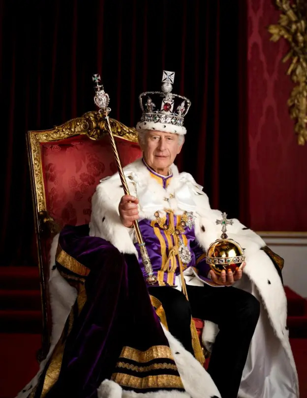 King Charles III in coronation robes, crown, sceptre and orb, seated on a throne