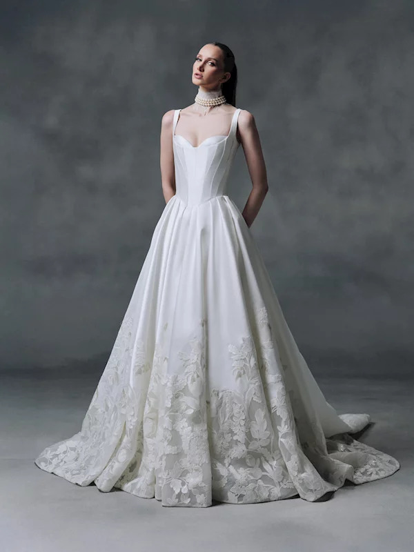 Woman in white bridal gown with lace hem standing in studio portrait