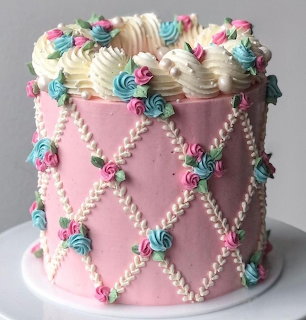 Pink cake decorated with pearl lattice pattern, pastel roses, and white cream dollops