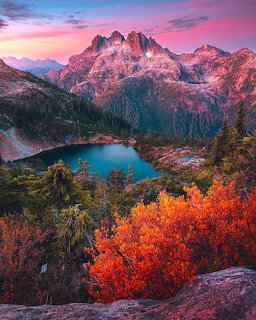 Alpine lake surrounded by fall foliage with jagged mountain peaks at sunset