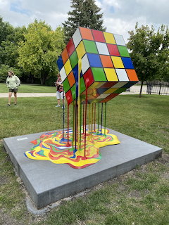 Colorful melting Rubik's Cube sculpture on a concrete pedestal in a park