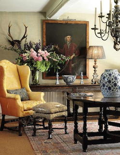 Country house interior with yellow wingback chair, oil portrait, flowers, antique furniture and blue white china