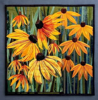Quilted fabric art showing yellow and orange coneflowers with dark centers on green stems in detailed textile work