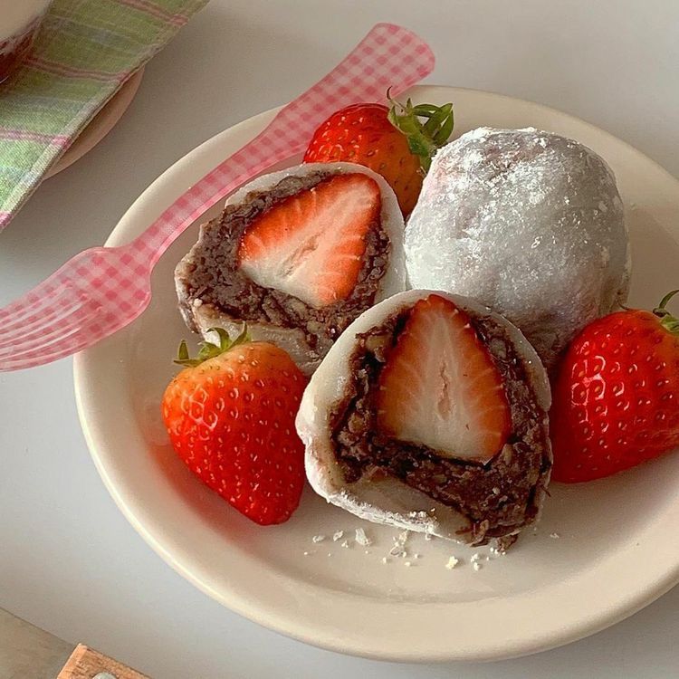 Strawberry daifuku mochi cut open on a white plate with fresh strawberries