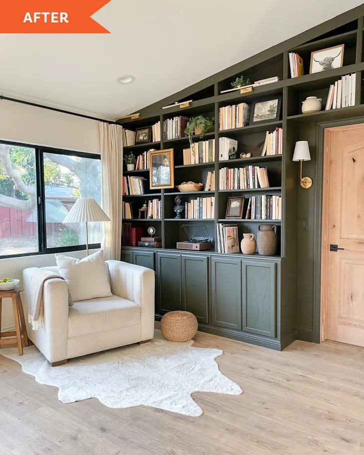 Cozy room with dark green bookshelves, white armchair, window, and light wood floor