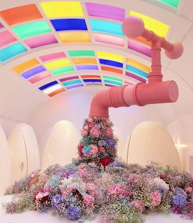 Colorful restroom interior with giant pink faucet, flowers, egg pods, and rainbow glass ceiling