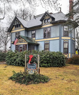 Light blue Victorian inn with ornate trim and front yard sign on cloudy day