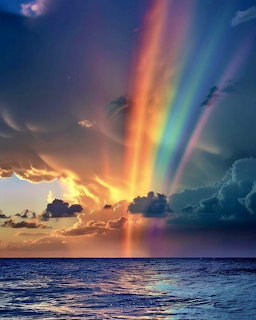 Colorful rainbow over ocean at sunset with dramatic clouds and light rays