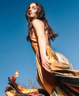Woman in orange dress photographed from below against blue sky