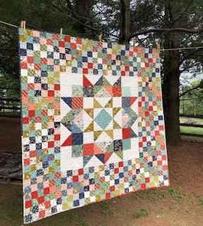 Colorful patchwork quilt with star pattern and checkerboard blocks hanging outdoors