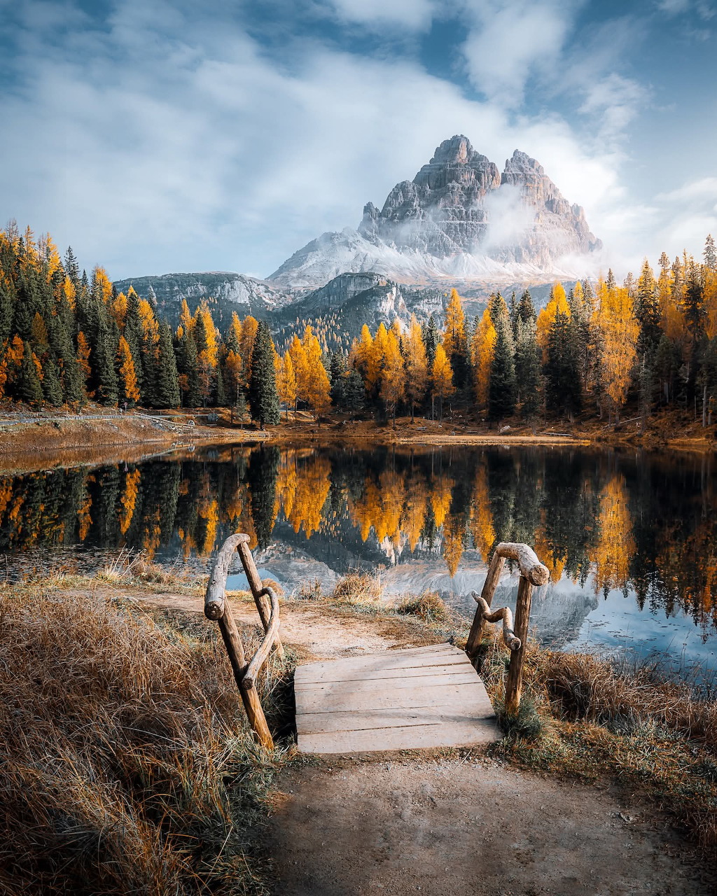 Wooden dock on a still alpine lake with golden autumn trees and a rocky mountain reflected in the water