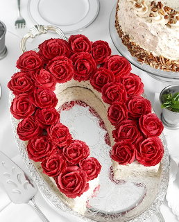 Number-shaped cake with red rose frosting and white icing on a dessert table