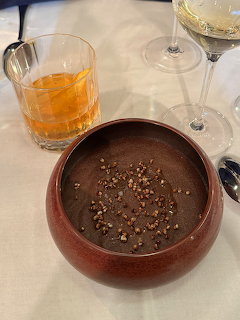 Chocolate dessert in brown bowl with nuts, orange cocktail and white wine on white tablecloth