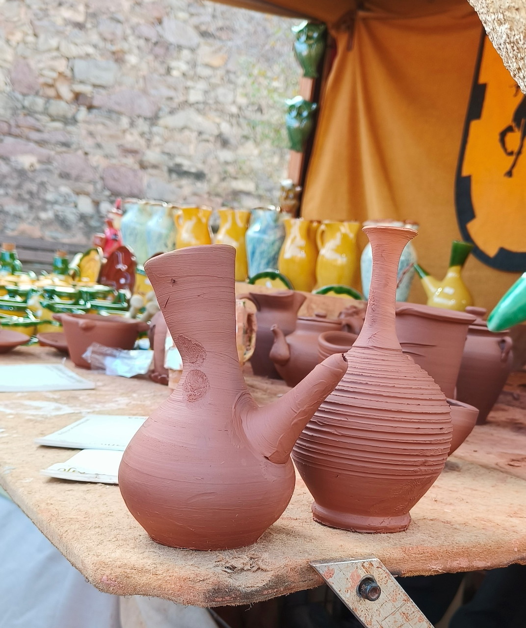 Two terracotta clay jugs and a ribbed vase on a wooden table at an outdoor pottery market