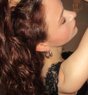 Side profile of a young woman with curly brown hair wearing a silver hoop earring and black lace top