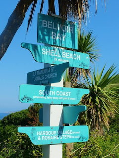 Teal directional signpost pointing to beaches and coastal locations with tropical plants and blue sky