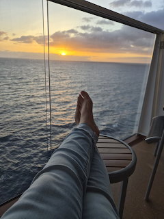 Person relaxing with feet up on a cruise balcony facing the ocean at sunset