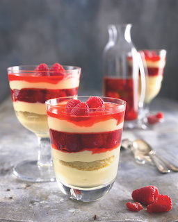 Two glass cups filled with colorful layered dessert topped with raspberries